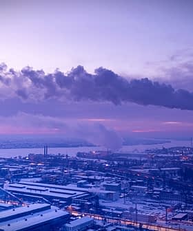 Industrial power plant with smoke rising from tall chimneys against a twilight sky. - Olive Oil Times