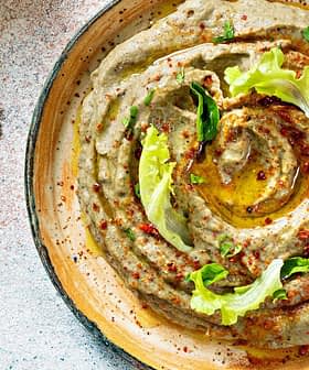 Bowl of hummus topped with olive oil, herbs, and spices, served with flatbread on the side. - Olive Oil Times