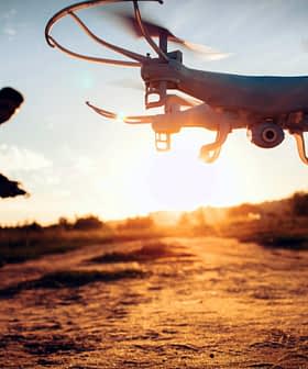 A drone flying in the foreground with a person operating it in the background during sunset. - Olive Oil Times