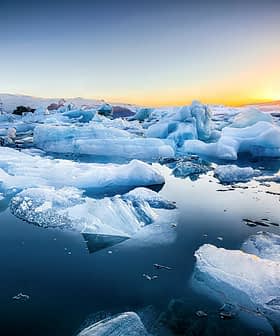 Icebergs of various shapes and sizes floating in calm water during sunset with a colorful sky. - Olive Oil Times