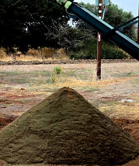 A pyramid-shaped mound of soil on a construction site with machinery in the background. - Olive Oil Times
