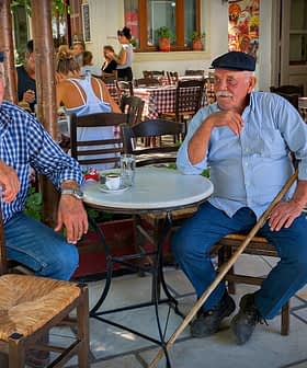 Two older men with hats sitting at a small round table in a café setting. - Olive Oil Times