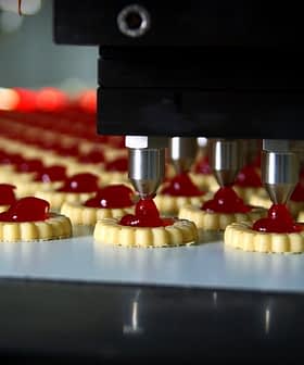 Automated machine dispensing red filling onto cookie bases in a production line. - Olive Oil Times