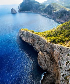 Aerial view of rocky cliffs meeting the blue ocean under a clear sky. - Olive Oil Times