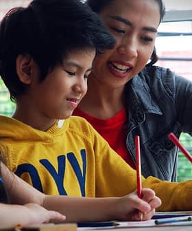 A woman assisting two children with drawing activities at a table. - Olive Oil Times