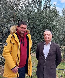 Two men posing for a photo in an olive grove with olive trees in the background. - Olive Oil Times