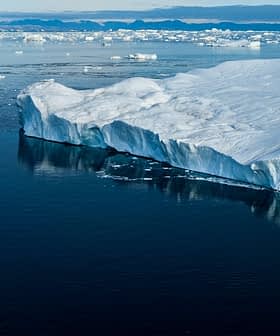 A large glacier edge with icebergs floating in calm water under a clear sky. - Olive Oil Times