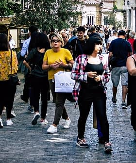 Group of people walking on a cobblestone street in an urban area with shops and trees. - Olive Oil Times