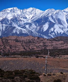 A view of snow-capped mountains rising above rocky terrain under a clear blue sky. - Olive Oil Times