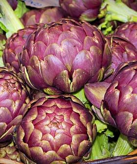 A basket filled with fresh purple artichokes, showcasing their rounded shape and green leaves. - Olive Oil Times