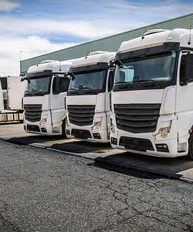 Four white delivery trucks parked in a row at a loading dock area. - Olive Oil Times