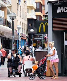 A street scene featuring a McDonald's restaurant and pedestrians, including a woman with a stroller and a man on a mobility scooter. - Olive Oil Times