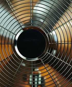 Close-up view of a metal oscillating fan with a wire grille and circular center. - Olive Oil Times