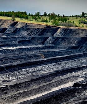 Aerial view of an open-pit mining site with layered black earth and machinery in the distance. - Olive Oil Times