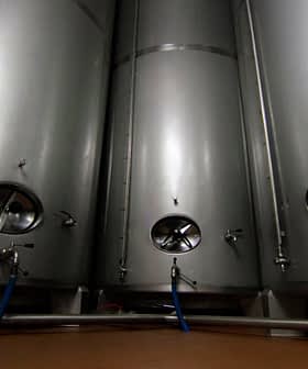 Three stainless steel fermentation tanks with circular openings and valves in a dimly lit space. - Olive Oil Times