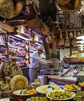 Interior of an Italian deli featuring various meats, cheeses, and a staff member slicing meat. - Olive Oil Times