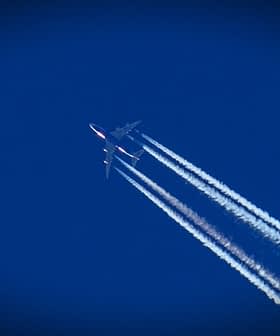 An airplane flying high in the sky, leaving behind white contrails against a blue background. - Olive Oil Times