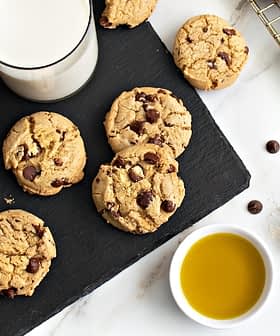Plate of chocolate chip cookies next to a glass of milk and a bowl of olive oil. - Olive Oil Times
