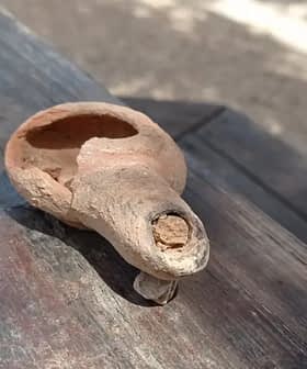 An ancient clay olive oil lamp with a spout and a round body resting on a wooden surface. - Olive Oil Times