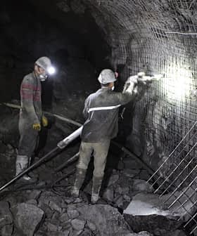 Two miners working in a dark underground mine with safety gear and tools. - Olive Oil Times