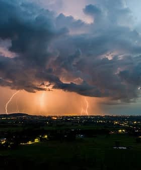 Lightning illuminating the sky over a landscape during dusk with dark clouds and distant lights. - Olive Oil Times