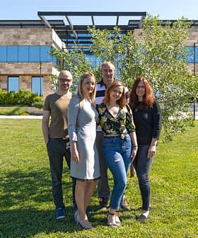 Five individuals standing together outdoors in front of a modern building with greenery. - Olive Oil Times