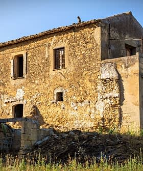 Abandoned stone house with a rustic exterior and overgrown vegetation in a rural area. - Olive Oil Times