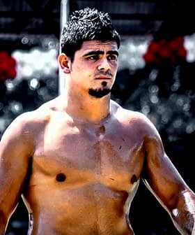 Shirtless male athlete with short dark hair standing outdoors, looking to the side. - Olive Oil Times