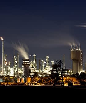 Night view of an industrial oil refinery with illuminated structures and smoke emissions from chimneys. - Olive Oil Times