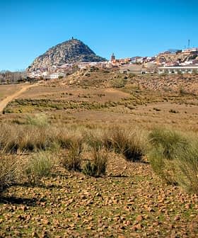 A landscape featuring a hill with a village at its base and dry vegetation in the foreground. - Olive Oil Times