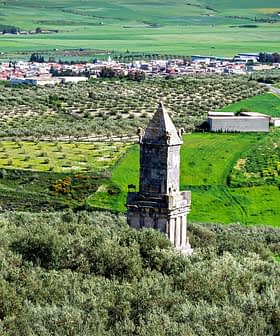 An ancient stone tower stands amidst olive groves and green fields in a rural landscape. - Olive Oil Times
