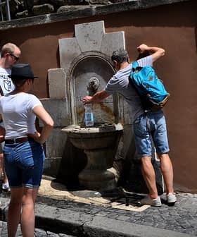 Group of people interacting with a wall-mounted fountain in an outdoor setting. - Olive Oil Times