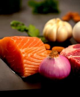 Raw salmon fillet, meat, onion, garlic, egg, and almonds arranged on a dark surface. - Olive Oil Times