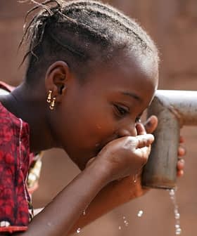 A child drinking water from a tap using cupped hands in a close-up view. - Olive Oil Times