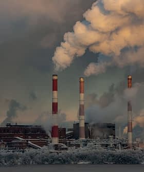 Industrial power plant with three tall smoke stacks emitting white smoke against a cloudy sky. - Olive Oil Times