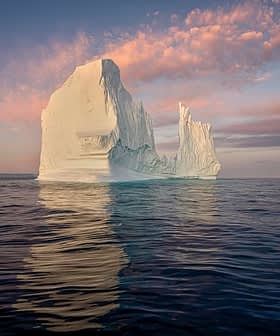 A large iceberg floating in calm water with a colorful sky at sunset. - Olive Oil Times