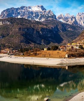 Scenic view of a lake reflecting mountains and a village in the foreground. - Olive Oil Times