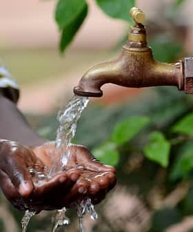 A person washing hands under a flowing tap with water in an outdoor setting. - Olive Oil Times