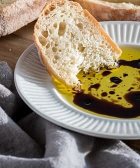 Slice of bread dipped in olive oil with balsamic vinegar on a white plate. - Olive Oil Times