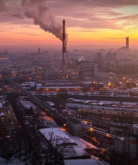 Aerial view of an industrial area with smoke stacks emitting smoke against a sunset sky. - Olive Oil Times