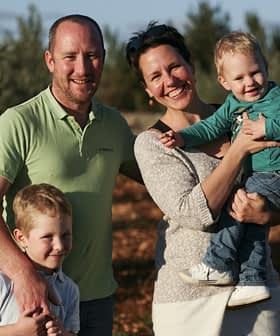 A family of four posing together in an olive grove, with two children and two adults smiling at the camera. - Olive Oil Times