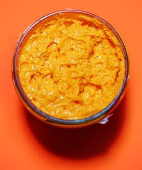 Glass jar filled with orange condiment on a bright orange background. - Olive Oil Times
