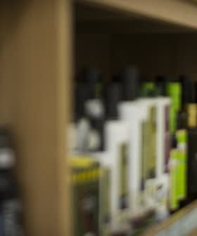 Various bottles of olive oil displayed on wooden shelves in a store. - Olive Oil Times