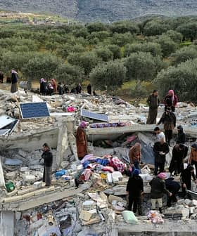 People searching through the rubble of a collapsed building surrounded by olive trees. - Olive Oil Times