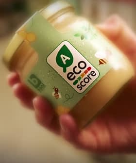 Hand holding a jar labeled with an eco score rating and a green logo. - Olive Oil Times