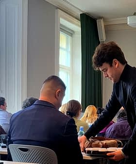 A young man serving food to a seated participant during a presentation on olfactory sensations. - Olive Oil Times