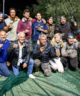 Group of individuals posing together with olive harvesting tools during nighttime. - Olive Oil Times