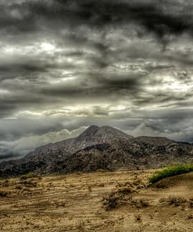 A mountain range under a dramatic cloudy sky with dark clouds and a barren landscape in the foreground. - Olive Oil Times