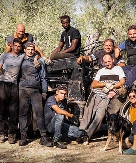 A group of twelve individuals posing together near an olive harvesting machine in an olive grove. - Olive Oil Times