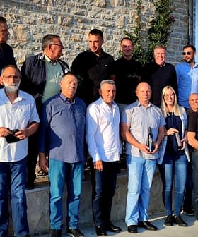 A group of individuals posing together outdoors in a casual setting, some holding bottles. - Olive Oil Times